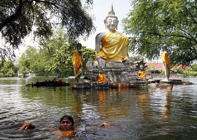 A boy swims near another flooded statue in the park as Thailand counts the cost of months of flooding. [Agencies]