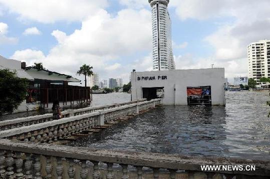 A local citizen walks on temporary wooden board above flooded water towards Si Phraaya Pier in Bangkok, Oct. 16, 2011. [Xinhua]