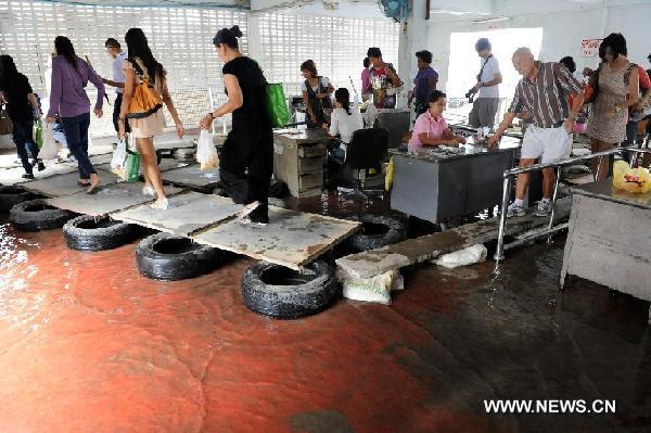 Local people and tourists walk on temporary wooden board above flooded water at Si Phraaya Pier in Bangkok, Oct. 16, 2011. [Xinhua]