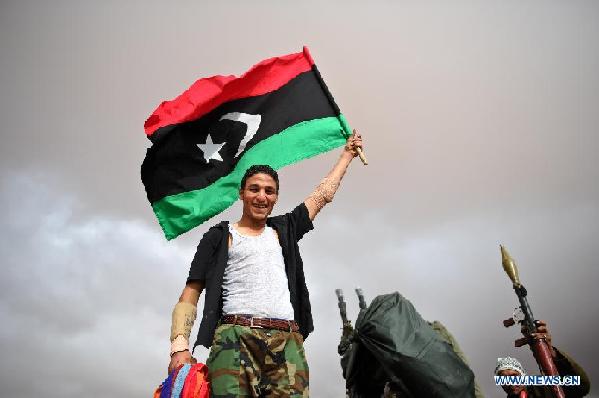 A National Transitional Council (NTC) fighter waves a flag outside a front line hospital in the suburbs of Bani Walid, Libya, Oct. 17, 2011. NTC fighters have controlled 90 percent area of Bani Walid, military spokesman Ahmed Bani said Monday. [Li Muzi/Xinhua]