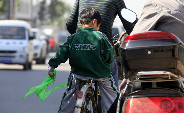 A pupil at a primary school of Weiyang district, Xi'an, who was told he had to wear a green scarf, takes it off as his family picks him up after lessons on Monday. [Provided to China Daily]