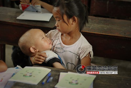 A left-behind girl sits in the class when coaxing her younger brother to sleep in the Good Friend Primary School, Fenghuang Town, Hunan Province. Their parents went out of town to work, so the girl has to bring her brother to school. 