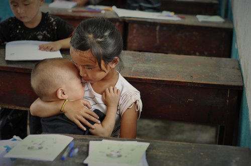 A left-behind girl sits in the class when coaxing her younger brother to sleep in the Good Friend Primary School, Fenghuang Town, Hunan Province. Their parents went out of town to work, so the girl has to bring her brother to school. 