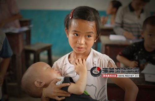 A left-behind girl sits in the class when coaxing her younger brother to sleep in the Good Friend Primary School, Fenghuang Town, Hunan Province. Their parents went out of town to work, so the girl has to bring her brother to school. 