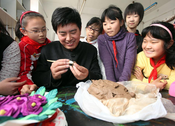 Zhang Yu (2nd L), the 6th generation of clay sculptor Zhang, demonstrates manufacturing process to students from Xinghua Primary School, in north China's Tianjin, Nov. 16, 2011. The first exhibition room of 'Clay figurine Zhang', the nation's non-material cultural heritage, opened in Xinghua Primary School.