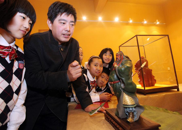 Zhang Yu (2nd L), the 6th generation of clay sculptor Zhang, presents art works to students from Xinghua Primary School, in north China's Tianjin, Nov. 16, 2011. The first exhibition room of 'Clay figurine Zhang', the nation's non-material cultural heritage, opened in Xinghua Primary School.