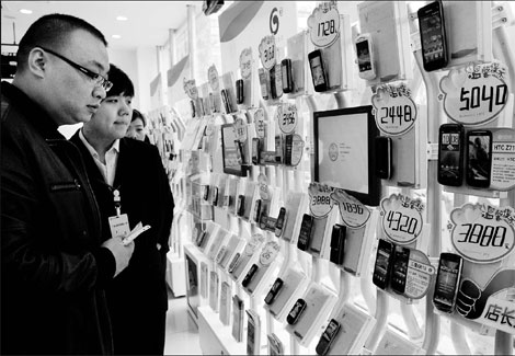 A salesman showing a customer different foreign and Chinese smartphones at a China Mobile shop in Zhengzhou, the capital city of Central China's Henan province. [Sha Lang/China Daily]