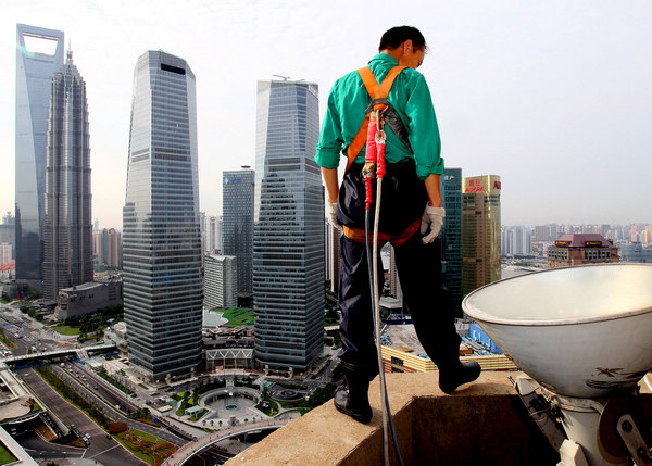 A migrant laborer who works as a cleaner stands on the ledge of a high-rise building in Shanghai's Pudong New Area on Aug 21. A recent survey finds that a very small number of young migrant workers are willing to go back home to a rural life. [Photo / Xinhua]