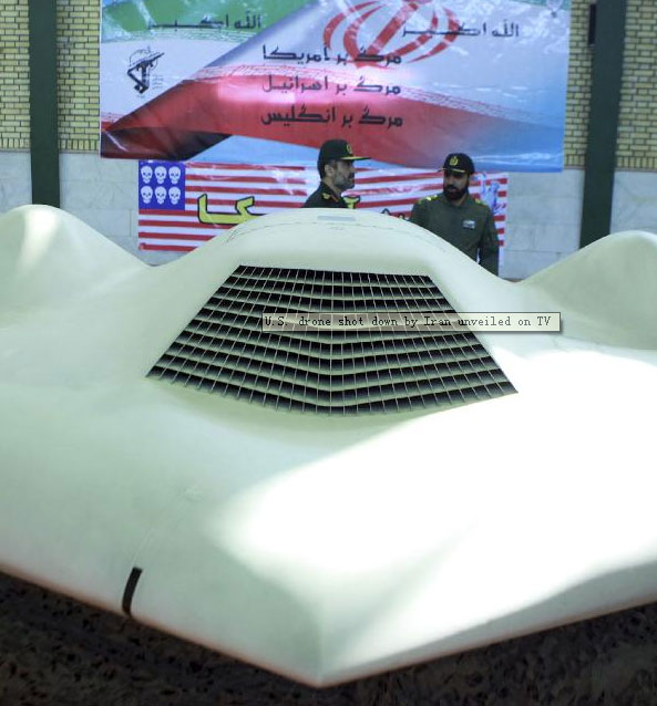 An undated picture received December 8, 2011 shows a member of Iran's revolutionary guard (R) and Amirali Hajizadehind, a revolutionary guard commander, standing behind the U.S. RQ-170 unmanned spy plane which is displayed in front of a flag with Persian script that reads 'Down with the U.S. (top), down with Israel and down with Britain (bottom)', at an unknown location in Iran. [Xinhua] 