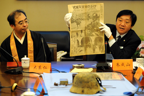 Zhu Chengshan, director of the Memorial Hall of the Victims in Nanjing Massacre by Japanese Invaders, presents a copy of the Asahi Shimbun newspaper, which was donated by a Japanese monk surnamed Ohigashi (left), who has given the memorial hall more than 1,000 items in the past. The paper, published on Dec 17, 1937, recorded how Japanese soldiers entered the city of Nanjing. 
