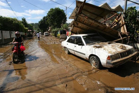 A resident passes by a house that rests on the top of a car after tropical storm Washi in Cagayan de Oro, the Philippines, on Dec. 20, 2011. National Disaster Risk Reduction and Management Council (NDRRMC) reported that as of Tuesday afternoon, the death toll from the typhoon stands at 957. Heavy downpour caused flooding and landslides that killed nearly 1,000 residents and displaced hundreds of families. [Rouelle Umali/Xinhua]
