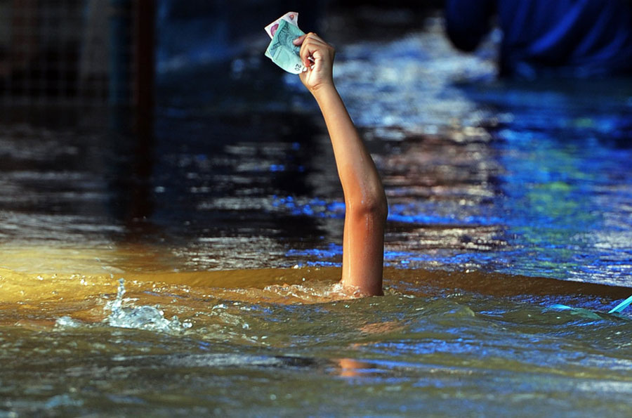 A boy holds aloft some banknotes as he battles surging floodwaters in Nonthaburi, near Bangkok, on Oct. 15, 2011. Since late July, the whole of Thailand, except for its southern region, has been afflicted by a disastrous deluge. The floods hit 65 out of 77 provinces and affected more than 13 million, or one in five Thai people. [Xinhua]