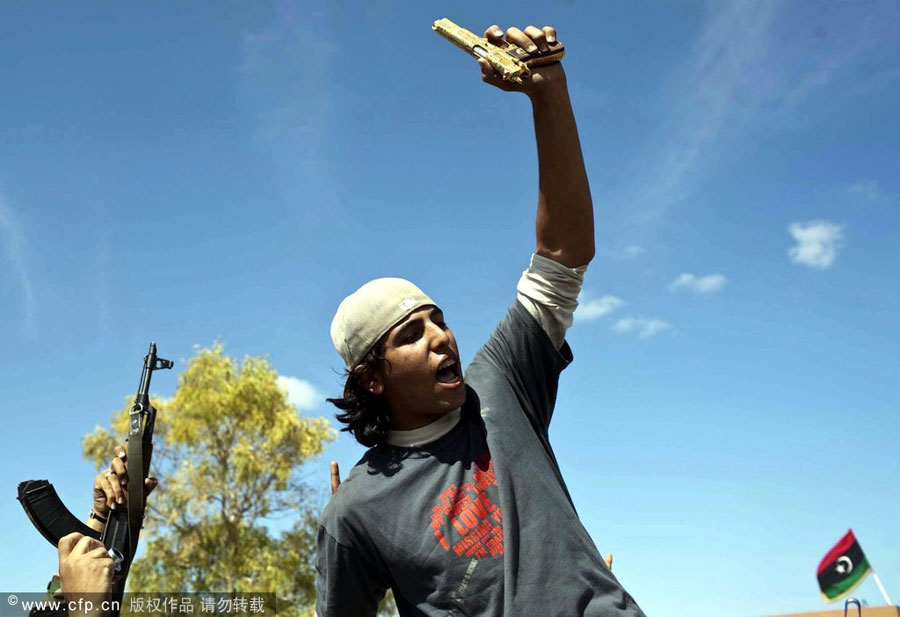 Twenty years old Libyan rebel fighter Mohamed El Bibi who allegedly found former Leader Muammar Gaddafi hiding in a hole in the ground, holds up a gold- plated gun that is said to have once belonged to Gaddafi, as he and his comrades celebrate former Leader's death and the fall of his stronghold town of Sirte, in Sirte , Libya, Oct. 20, 2011. [CFP]