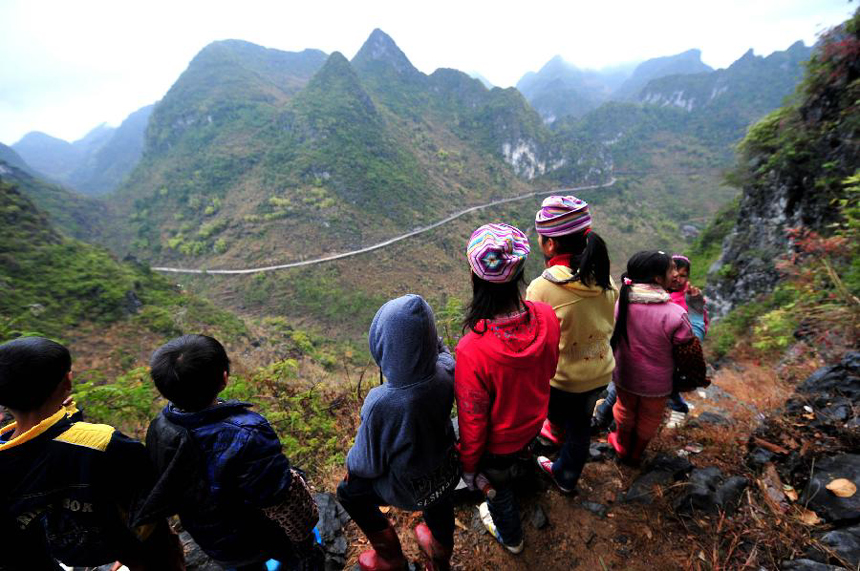 Children look at the highway in the distance while stopping at the mountain road on their way to school at Minxin Village of Mashan County in southwest China's Guangxi Zhuang Autonomous Region, Jan. 6, 2012. Every day, they have to leave home very early in the morning and climb over hills for hours to go to school. 