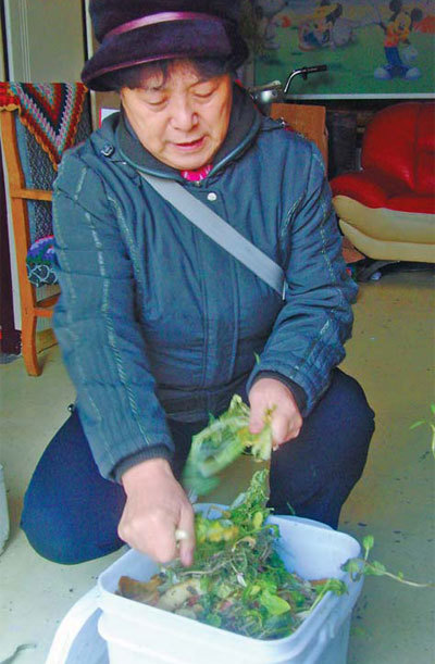 Sun Xiuli tosses vegetable leftovers into a bucket and sprinkles them with enzymes, as one of the participants of a garbage recycling project in Tianjin. [China Daily] 