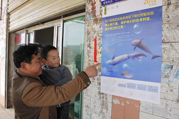 A poster urging villagers to cease electrofishing and protect the finless porpoises attracts the attention of Zhao Yihui and his nephew in Dongting village, Hunan province, on Saturday. [China Daily]
