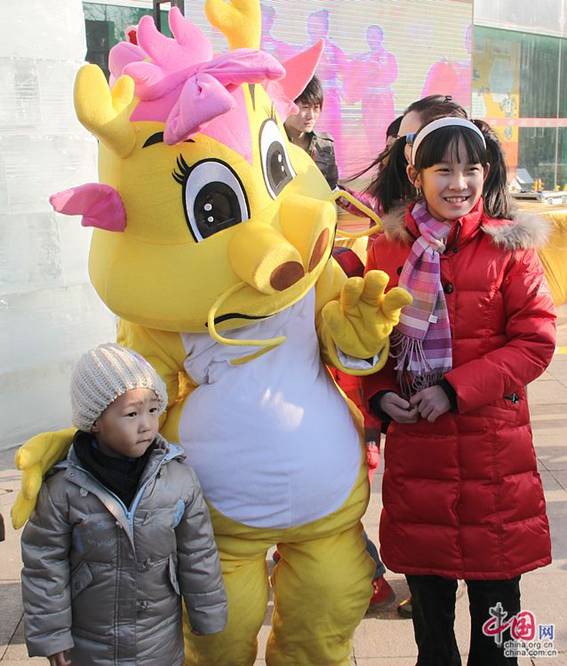 Two Chinese children are taking a group photo with a dragon mascot in a Spring Festival temple fair in Chaoyang Park, Beijing.两名中国儿童在北京朝阳公园的庙会上与小龙吉祥物合影。