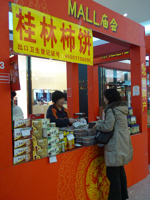 A customer is purchasing local snacks in an indoor temple fair in the Golden Resources Shopping Mall located in the northwest part of Beijing during the Spring Festival 2012, where visitors can enjoy the charm of the traditional Chinese arts and the delicacy of local snacks. [By Xu Lin / China.org.cn]