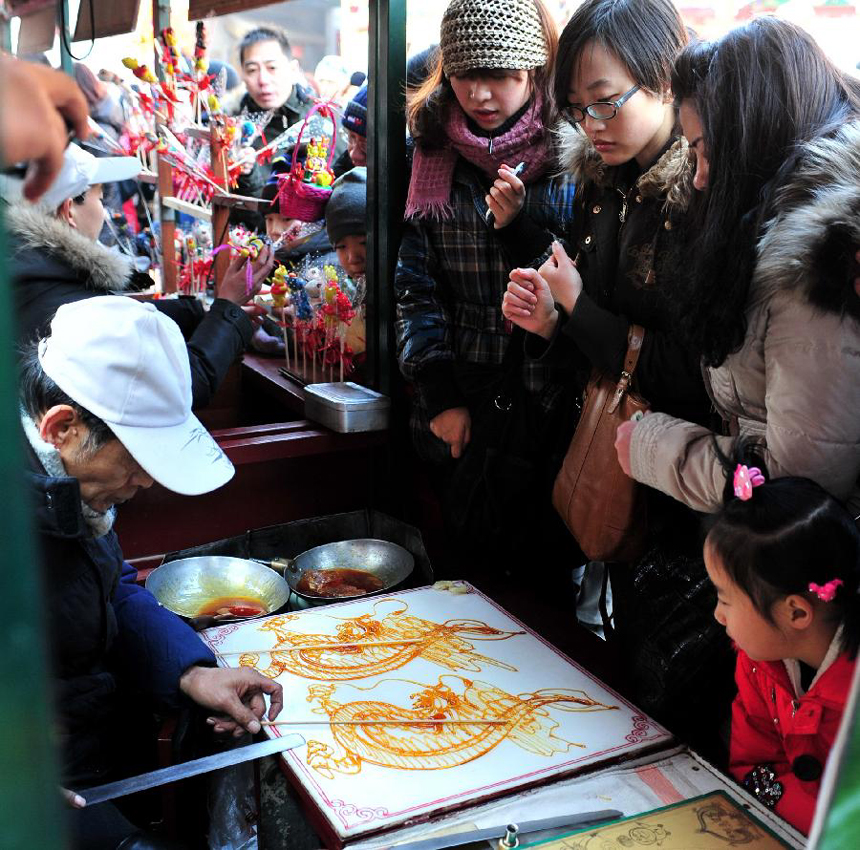 People watch the making of dragon-shaped sugar paintings at a temple fair held during the Spring Festival holiday in Tianjin, north China, Jan. 25, 2012. The Spring Festival, or the Chinese Lunar New Year, which fell on Jan. 23 this year, marked the start of the Year of Dragon, according to the Chinese zodiac. [Xinhua photo]