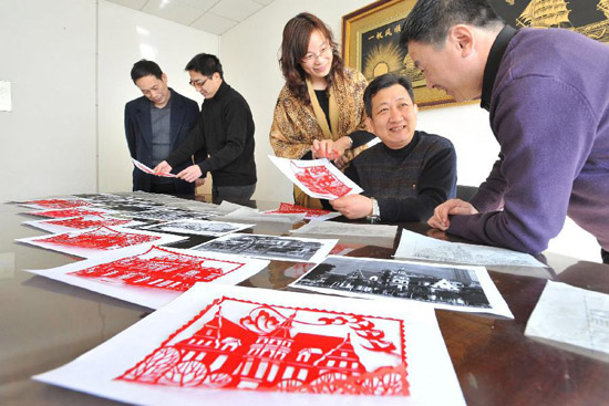 Li Qiang (2nd R), a kirigami artist, shows his paper-cutting work with the theme of western-style houses to his friends in Tianjin Municipality, north China, Feb. 17, 2012. A series of paper-cutting craftworks with the theme of western-style houses were created by local artists recently, to display the history and culture of the city. (Xinhua/Wang Xiaoming)