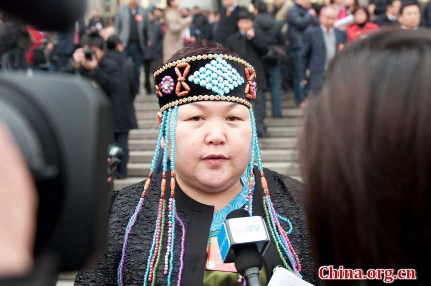 A delegate with Chinese ethnic group talks to TV reporters as she walks out of the Great Hall of the People in Beijing, China on Monday, March 5. [China.org.cn]