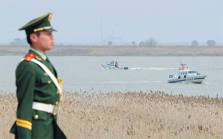 Police speedboats patrol the Qingcaosha Reservoir, which supplies 70 percent of the tap water in Shanghai, while an officer stands guard on Thursday. [China Daily] 