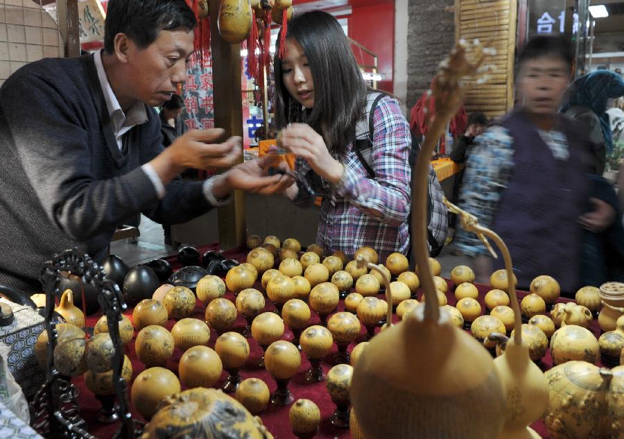 A tourist buys engraving works in Dunhuang, northwest China's Gansu Province, April 30, 2012. As tourism industry booms in Dunhuang, more than 500 folk artists have been attracted to develop their businesses in Dunhuang, which is well known for its Mogao Caves (Caves of 1,000 Buddhas), Crescent Lake and Mingsha Mountain. (Xinhua/Gao Jianjun) 