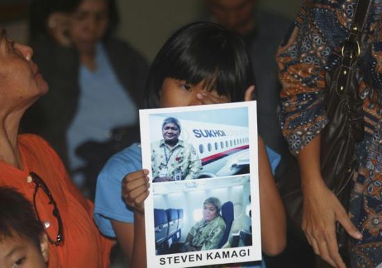 Tasya Kamagi, 10, holds the pictures of his father Steven that were taken when he boarded a Russian-made Sukhoi Superjet-100 that crashed on a mountainous area in West Java, at Halim Perdanakusuma Airport in Jakarta, Indonesia, Thursday, May 10, 2012.