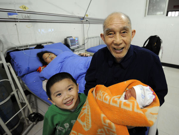A 75-year-old father, who only gave his surname as Shi, holds his newborn daughter with his son, aged 3, while his wife, 42, lies in bed at a hospital in Chongqing on Tuesday. The infant is the couple's third child and the man's fourth. His first child, a daughter, is 57 years old, and her mother died before Shi remarried.[ Photo / China Daily ]
