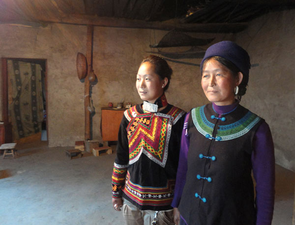 Waqi Wuji (left) and her mother Jida Geguo in their poorly furnished living room. The young woman has to help her mother support the family after her father died of an AIDS-related illness. [ Photo / China Daily ]