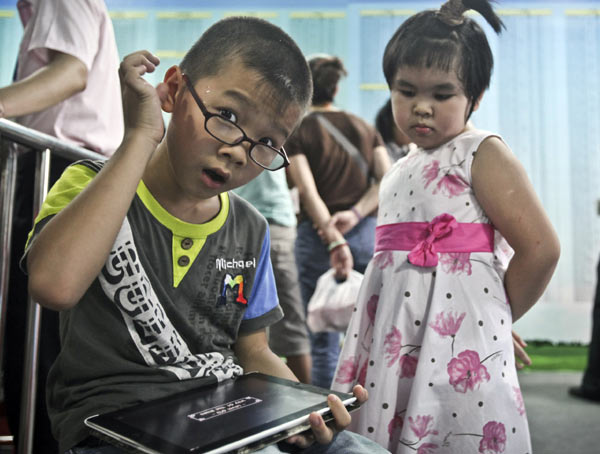 A boy plays with a tablet while waiting for his parents at a sales office in Guangzhou, South China's Guangdong province. [ Photo / China Daily ]