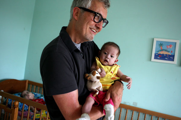 Tim Baker cradles a child at the Shepherd's Field Children's Village in Tianjin. [ Photo / China Daily ]