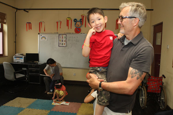 Tim Baker carries an orphan at the Shepherd's Field Children's Village in Tianjin. Photos by Jiang Dong / China Daily