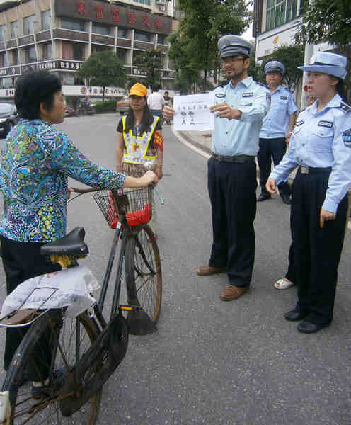 Josh Garcia, a temporary chengguan from the US, shows a pedestrian a sign saying 'please do not jaywalk' in Zhuzhou, Hunan province, last week. [Yang Lingling / For China Daily]    