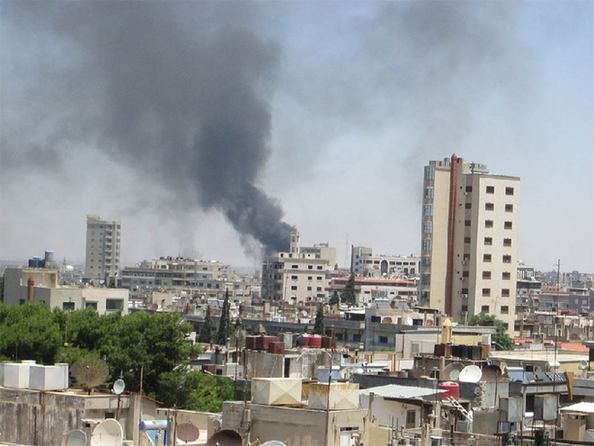 Smoke drifts into the sky from buildings and houses hit by shelling in Homs, Syria. [David Manyua/UN Photo]