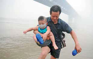 A masked Shen Yanwei gets a helping hand from his grandfather as they play on the banks of the Yangtze River in Wuhan, Hubei province, on Monday.[China Daily]