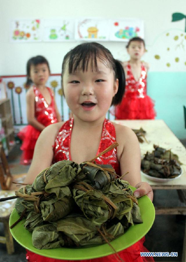 A young girl, whose parents have left hometown to work in cities, shows Zongzi, a pyramid-shaped dumpling made of glutinous rice wrapped in bamboo or reed leaves, in Gaoqing County, east China's Shandong Province, June 22, 2012. Many volunteers came to make Zongzi for these left-behind children to greet the upcoming Chinese Dragon Boat Festival, which falls on June 23 this year. [Xinhua]