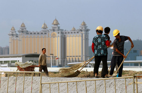 Workers clean a road at a construction site with a building of Macau seen in the distance in Hengqin Island, Zhuhai city, Guangzhou province on June 15, 2012. [Photo/CFP] 