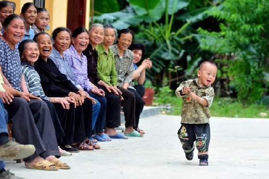A boy plays in front of people at a center for the aged in Longfu village, Du'an Yao autonomous county, Southwest China's Guangxi province, June 27, 2012. [Photo/Xinhua]