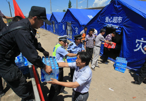 Policemen and relief workers move bottled water into a tent in Xinyuan county, Northwest China’s Xinjiang Uygur autonomous region, July 2, 2012. [Photo/Asianewsphoto]