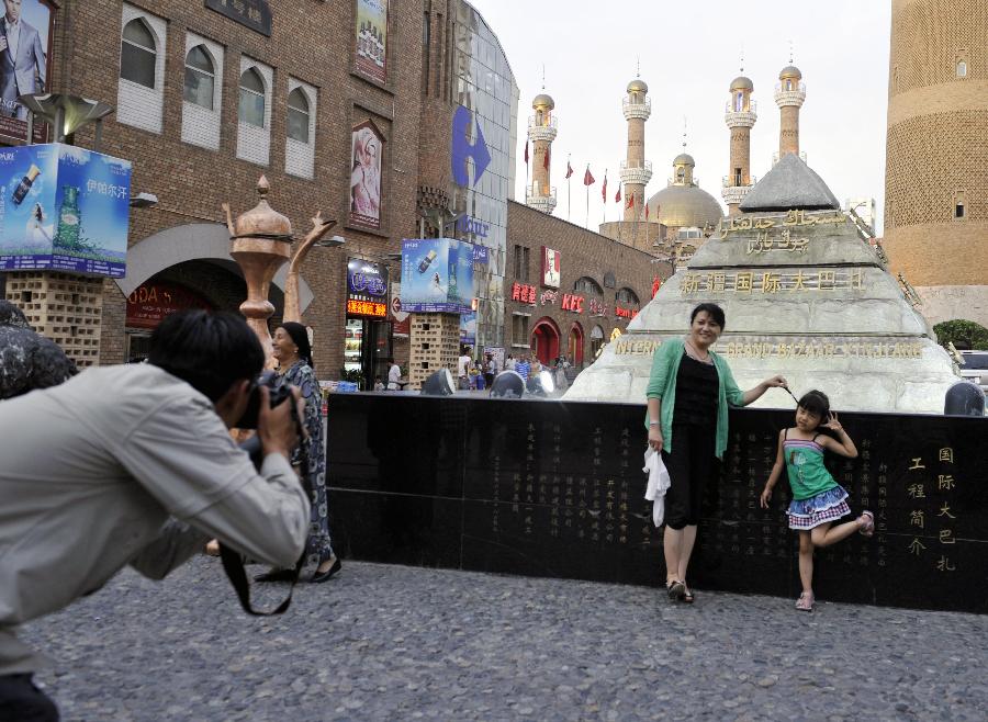 Tourists pose for photo in Xinjiang International Grand Bazaar in Urumqi, northwest China's Xinjiang Uygur Autonomous Region, July 2, 2012. As travel season is coming, Xinjiang International Grand Bazaar attracts quite a lot tourists. (Xinhua/Zhao Ge) 