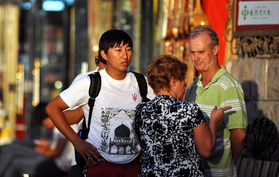 Two foreign tourists discuss their travel route with a tour guide in Xinjiang International Grand Bazaar in Urumqi, northwest China's Xinjiang Uygur Autonomous Region, July 2, 2012. As travel season is coming, Xinjiang International Grand Bazaar attracts quite a lot tourists. (Xinhua/Zhao Ge) 