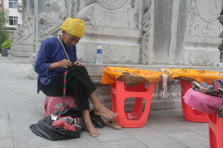 An elderly woman makes and sells her handicrafts to visitors on June 28. [CnDG by Jiao Meng]