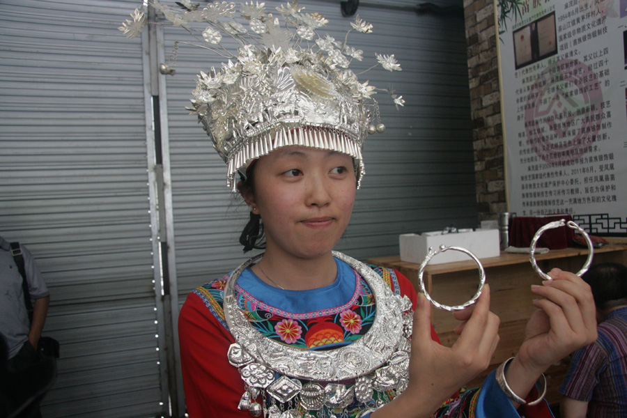 A girl wearing traditional Miao silver jewels displays newly-produced silver bracelets on June 28. The Miao ethnic minority is well-known for their uniquely designed hand-made jewelry. [CnDG by Jiao Meng]