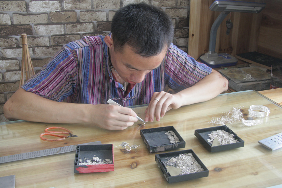 A handicraftsman wiredraws a silver piece in Fenghuang (phoenix) ancient town, central China’s Hunan Province on June 28. The Miao ethnic minority is well-known for their uniquely designed hand-made jewelry. [CnDG by Jiao Meng]