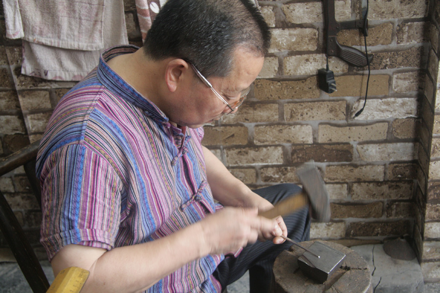 A handicraftsman forms a silver strip into a bracelet in Fenghuang (phoenix) ancient town, central China’s Hunan Province on June 28. The Miao ethnic minority is well-known for their uniquely designed hand-made jewelry. [CnDG by Jiao Meng]