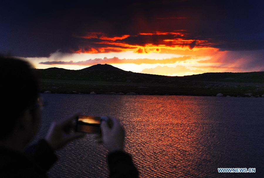 A visitor takes pictures of the sunset in Qiangtang Grassland in Nagqu, southwest China's Tibet Autonomous Region, July 4, 2012. The magnificent scenery of Nagqu area in July attracts quite a lot of tourists.