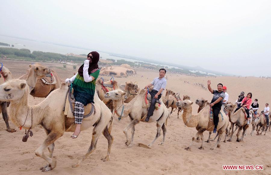 Tourists ride camels in the Sand Lake scenic area in Pingluo County, northwest China's Ningxia Hui Autonomous Region, July 8, 2012. Scenic spots in the deserts of Ningxia have entered the high season of tourism in recent days. [Xinhua/Li Ran]