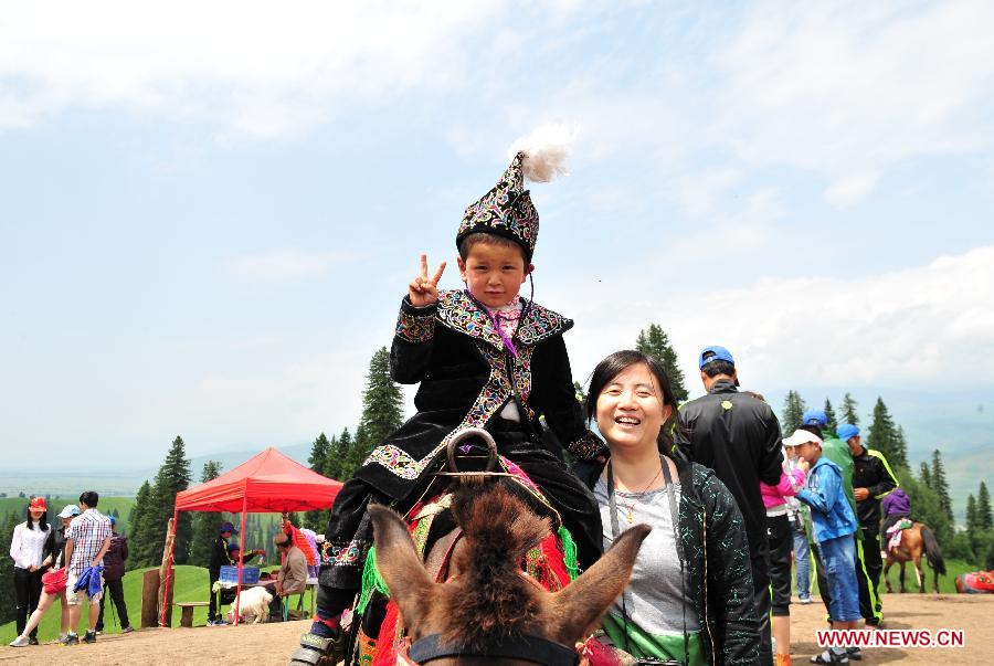 Tourists poses for a photo with Kazak boy at the Narat grassland scenic area, northwest China's Xinjiang Uygur Autonomous Region, July 5, 2012. Xinjiang entered the peak season for summer tourism recently with glamorous sceneries of snowy mountains, deserts, lakes and pastures. (Xinhua/Zhang Jiansong)