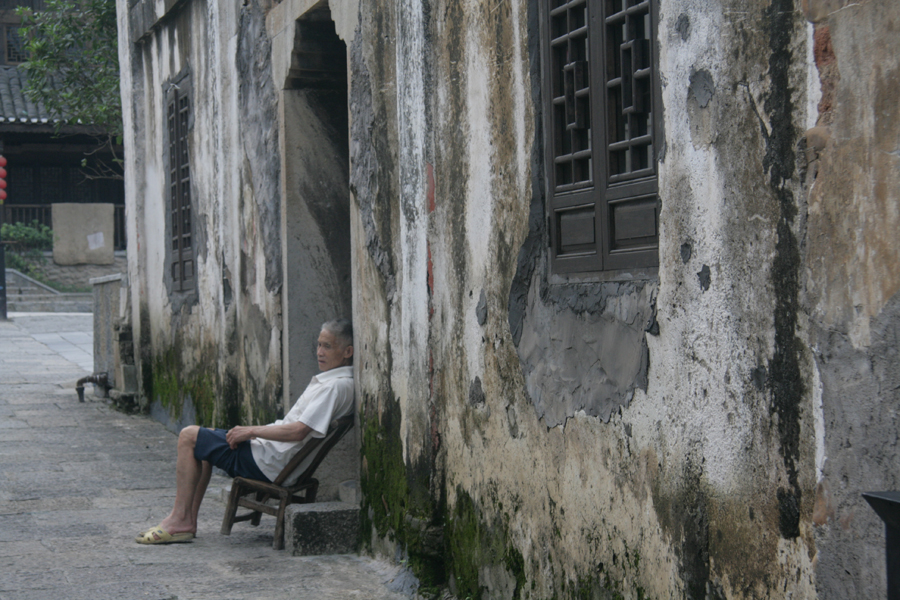 An elderly man rests in front of his old house. [CnDG by Jiao Meng]